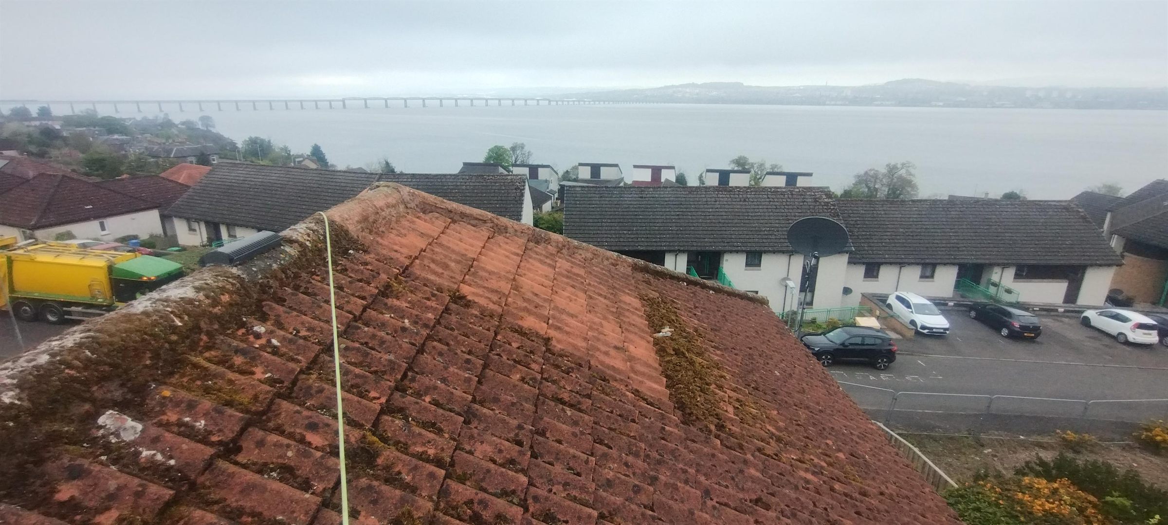 Pantile roof cleaned down — A thick mat of moss holding damp against the tiles, cleared back to sound pantiles. That is the Tay Road Bridge behind.